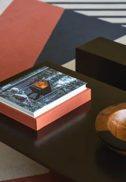 A close-up of a coffee table book titled 'Cabin Fever' on a dark table next to a wooden bowl, with a geometric rug visible.